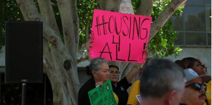 IMage of people protesting holding up signs saying Housing for All