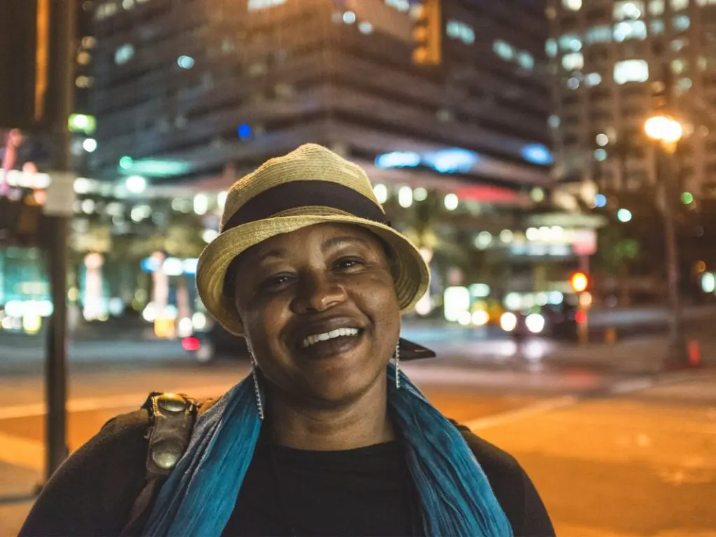 Smiling woman in a hat standing in downtown Los Angeles at night