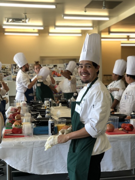 chef smiling at the camera in a crowded kitchen