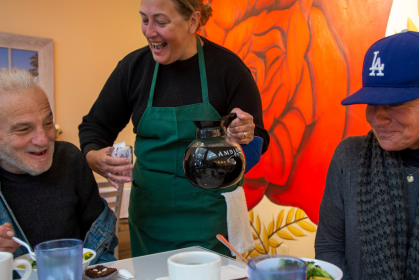 Woman serving coffee to two smiling people