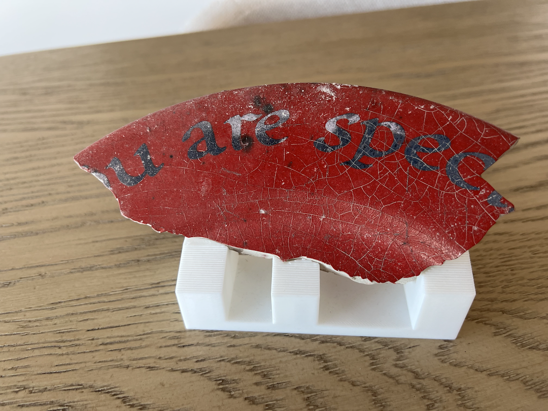 A small red fragment recovered from wildfire debris, showing cracks, burn marks, and partial printed text.