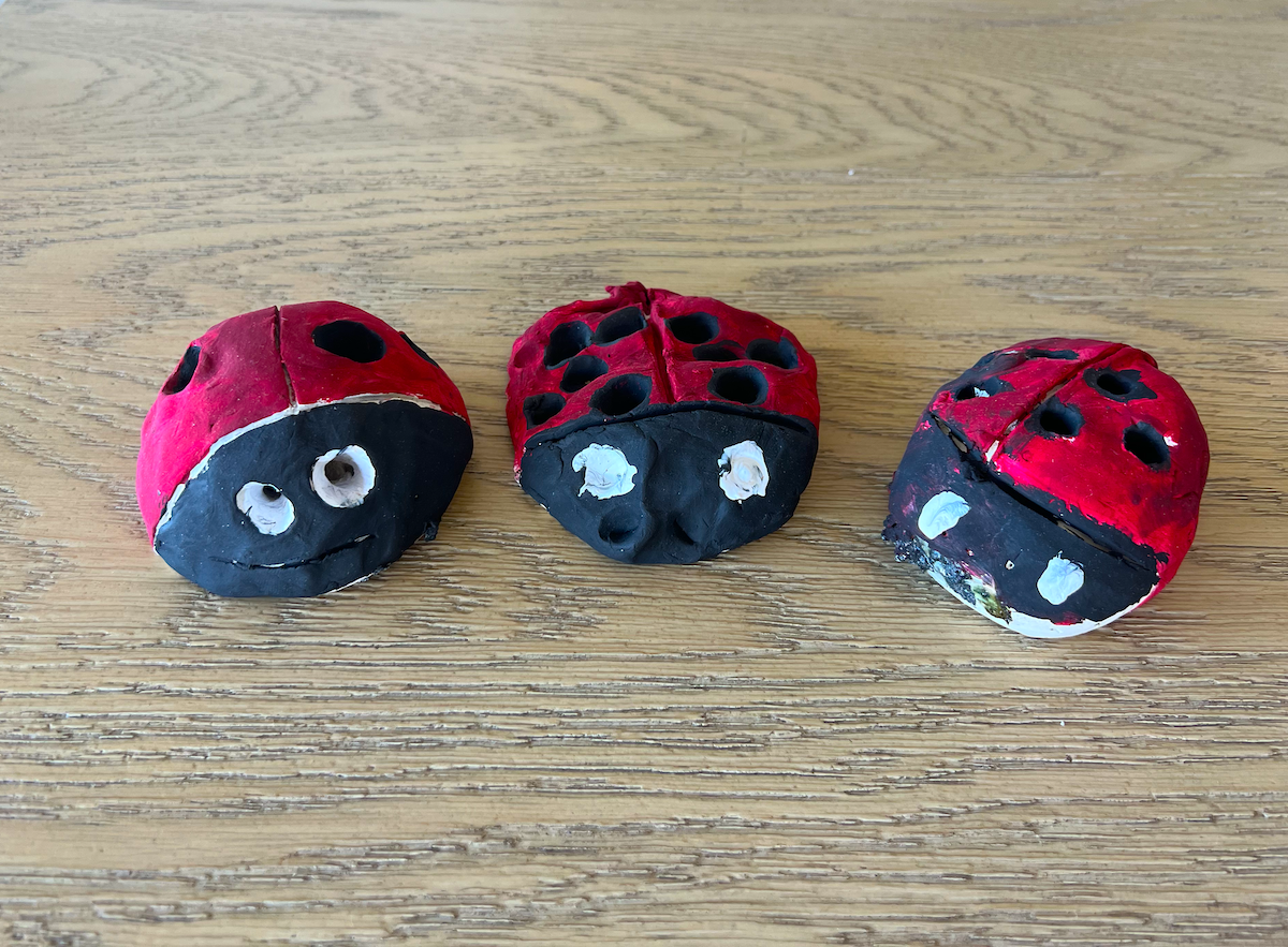 Three small red and black clay ladybug pencil holders made by Jocelyn’s children, resting on a wooden surface.