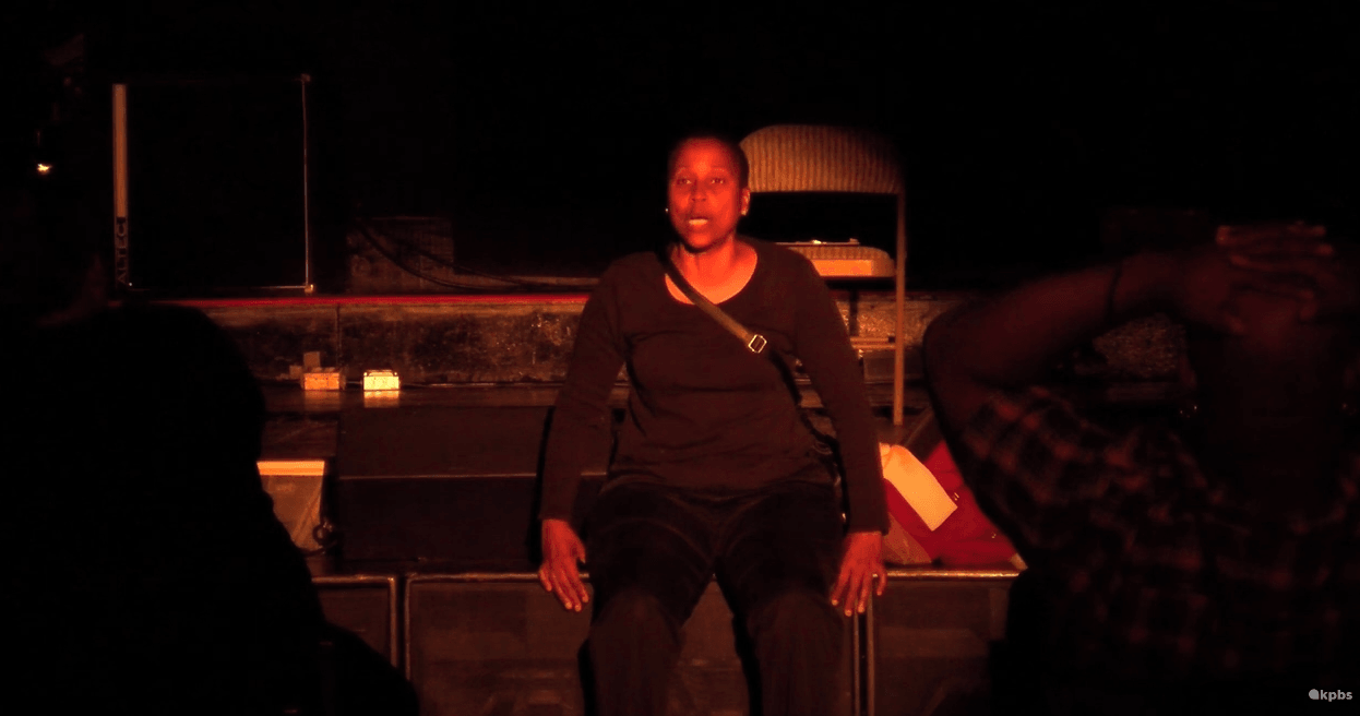 Renee Westbrook seated on stage under red lighting during a performance.