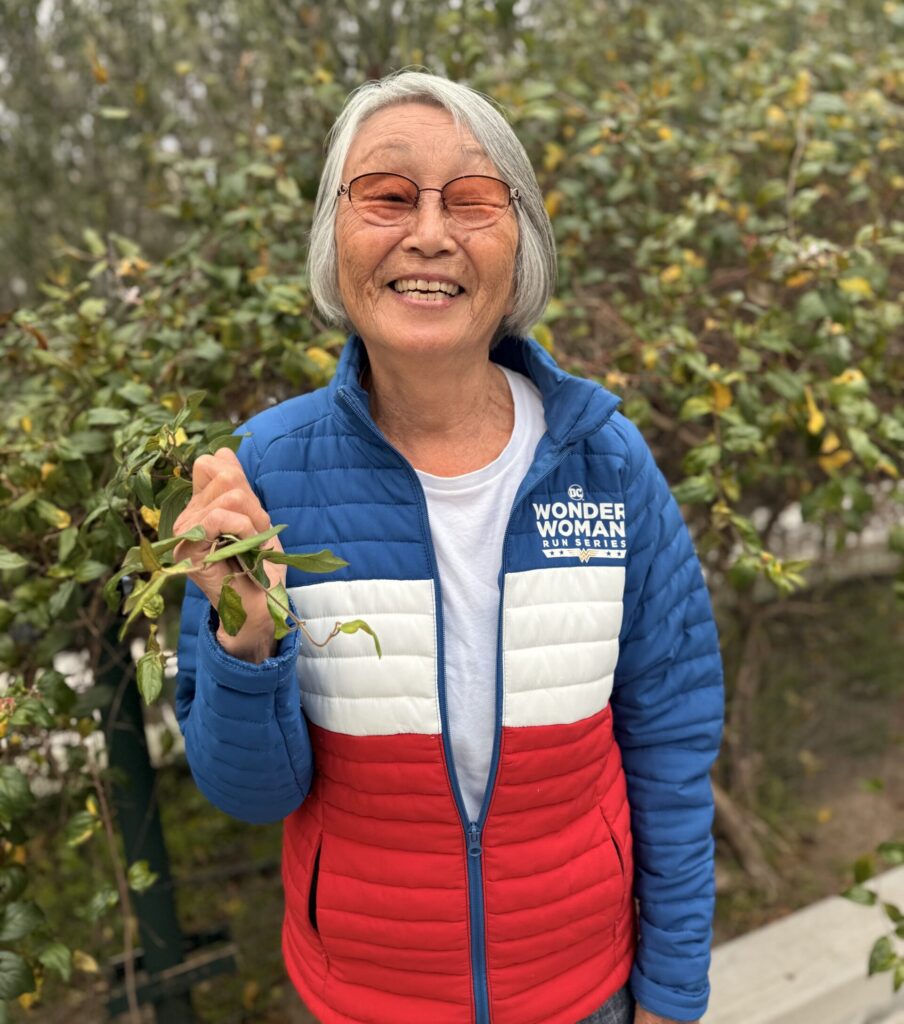 Emi Carvell, St. Joseph Center volunteer and Master Gardener, standing outdoors among greenery.