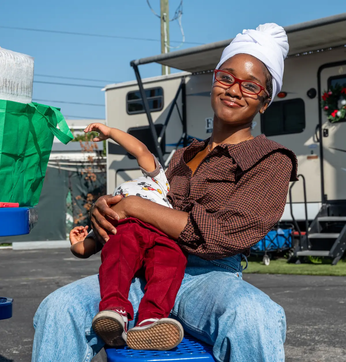 Nandi sits outdoors holding her child during a St. Joseph Center community event, reflecting connection, support, and family stability.